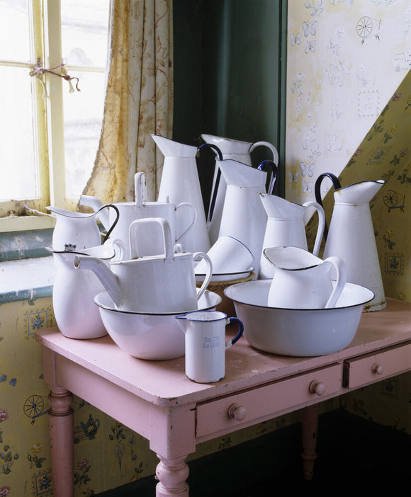 A group of enamel jugs and basins on a pink table by a window at Tyntesfield