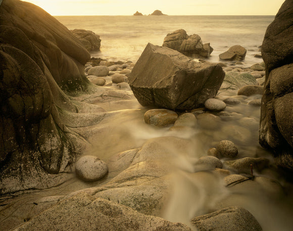 A rock nestled in a crag on the beach at Cape Cornwall with the tide running past, out to the sea