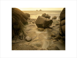 A rock nestled in a crag on the beach at Cape Cornwall with the tide running past, out to the sea