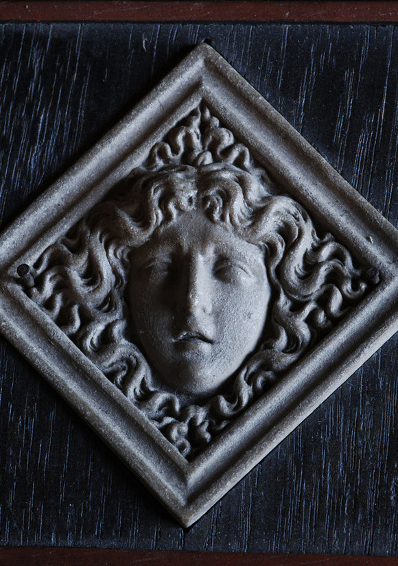 A framed, diamond-shaped stone head, possibly representing Medusa, from Admiral at Snowshill Manor