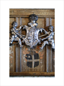 Carved coat-of-arms hang above a painted coat-of-arms on the wooden panellling, part of the Charles Wade collection at Snowshill Manor, Gloucestershire