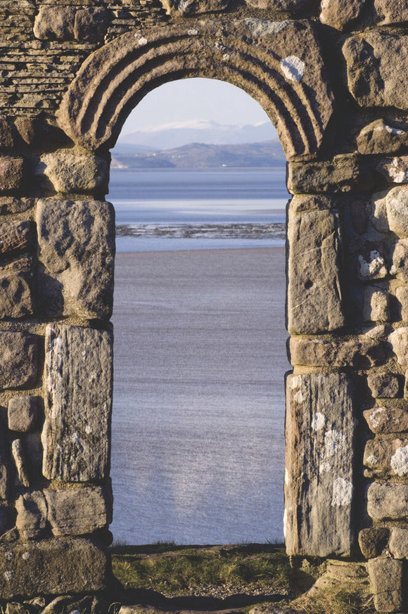 A view through one of the carved stone arched windows of St Patricks Chapel, Heysham Head, looking towards Morecambe Bay, Lancashire