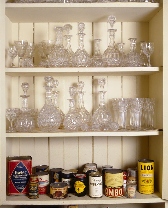 Cut glass decanters on two shelves with tins and groceries on the bottom shelf in a pantry cupboard at Tyntesfield