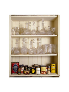 Cut glass decanters on two shelves with tins and groceries on the bottom shelf in a pantry cupboard at Tyntesfield