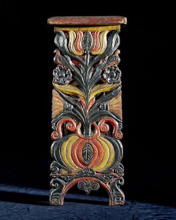 Detail of a small bench end in the Outer Hall at Dunster Castle which is intricately carved and painted in a floral design