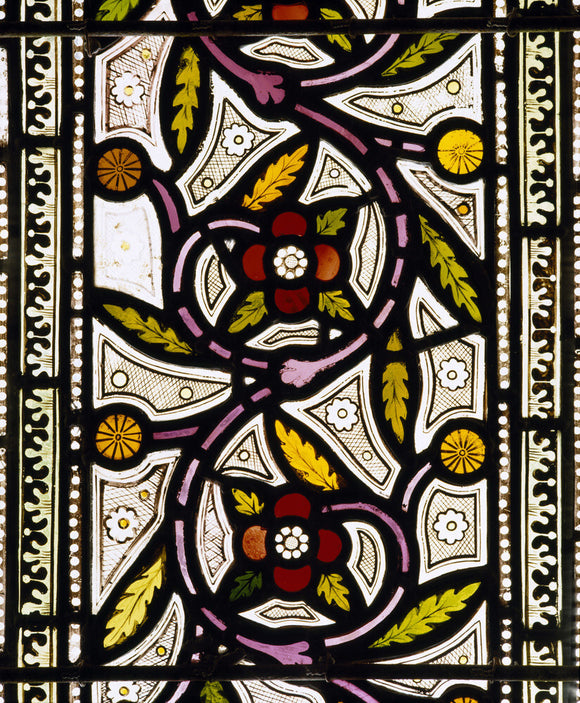 A stained glass window in the Chapel at Tyntesfield depicting a floral scroll in reds and greens
