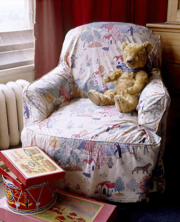 Lord Wraxall's Teddy Bear sitting on a chair with a nursery print cover, with a drum and a box of toys in front, at Tyntesfield