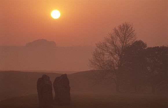 Sunrise at Avebury with the stones rising out of the morning mist and a deep orange sky behind