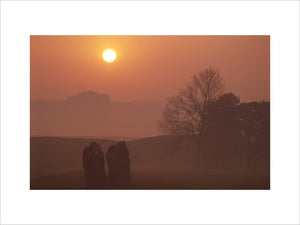 Sunrise at Avebury with the stones rising out of the morning mist and a deep orange sky behind