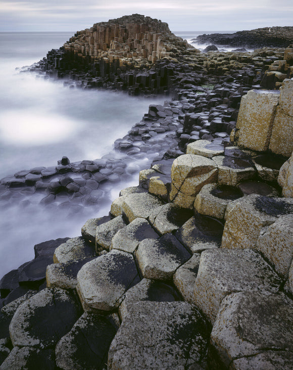 A view of the unusual rock formations at Giant's Causeway, taken under a dark forboding sky and with a blur of crashing waves