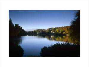 A mirror-like surface on the lake at Stourhead, Wiltshire with autumnal trees reflected in the water