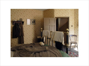 A view of the 1930s house bedroom at the Birmingham Back to Backs showing the bed and bedstead with a coat spread over it for additional warmth